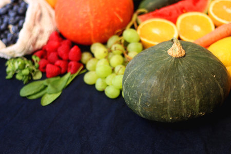 Round straw bag and various seasonal fruits and vegetables on dark background. Summer and fall produce. Selective focus.の写真素材