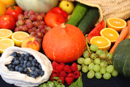 Round straw bag and various seasonal fruits and vegetables on dark background. Summer and fall produce. Selective focus.の写真素材
