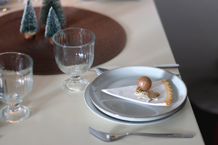 Table set for Christmas meal with plates, glasses, holiday decorations, lit candles and wine. Selective focus.の写真素材