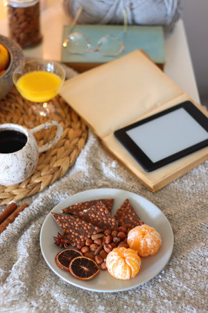Books, e-reader, tea, orange juice, fruit, snacks, yarn, blanket and lit candles on the table. Autumn or winter hygge at home. Selective focus.の写真素材