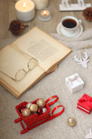 Various Christmas decorations, lit candles, cup of tea or coffee, cookies, books, presents and soft blanket on the table. Holiday hygge at home. Selective focus.の写真素材