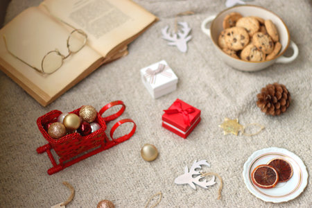 Various Christmas decorations, lit candles, cup of tea or coffee, cookies, books, presents and soft blanket on the table. Holiday hygge at home. Selective focus.の写真素材