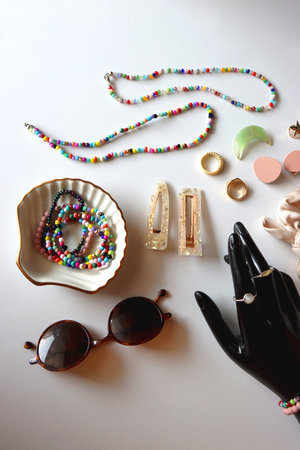 Hand figurine, sunglasses, gold jewelry, colorful bead jewelry, statement rings and various hair accessories on the white table. Flat lay.の写真素材