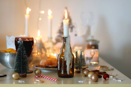Various Christmas decorations, cookies, chocolate, nuts and tangerines, wine glasses and lit candles on the table. Holiday hygge at home. Selective focus.の写真素材
