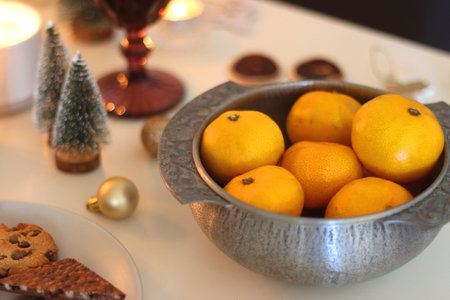 Various Christmas decorations, cookies, chocolate, nuts and tangerines, wine glasses and lit candles on the table. Holiday hygge at home. Selective focus.の写真素材