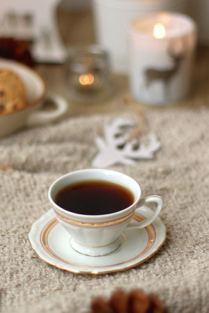Various Christmas decorations, lit candles, cup of tea or coffee, cookies, books, presents and soft blanket on the table. Holiday hygge at home. Selective focus.の写真素材