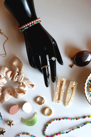 Hand figurine, sunglasses, gold jewelry, colorful bead jewelry, statement rings and various hair accessories on the white table. Flat lay.の写真素材