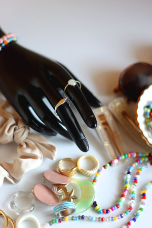 Hand figurine, sunglasses, gold jewelry, colorful bead jewelry, statement rings and various hair accessories on the white table. Selective focus.の写真素材