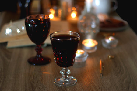 Books, lit candles, red wine, snacks and various decoration on the table. Dark academia or Halloween concept. Selective focus.の写真素材