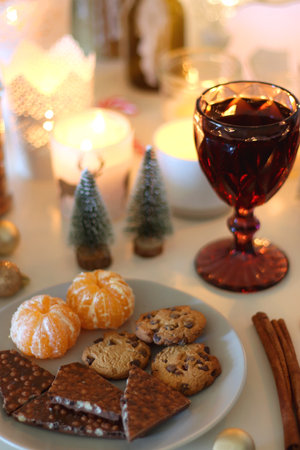Various Christmas decorations, cookies, chocolate, nuts and tangerines, wine glasses and lit candles on the table. Holiday hygge at home. Selective focus.の写真素材