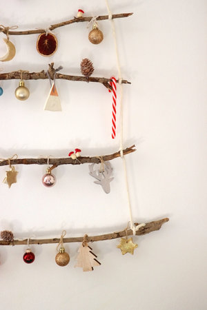 Creative DIY Christmas tree made with branches and decorated with various Christmas ornaments, hanging on the wall.の写真素材