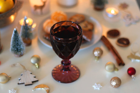 Various Christmas decorations, cookies, chocolate, nuts and tangerines, wine glasses and lit candles on the table. Holiday hygge at home. Selective focus.の写真素材