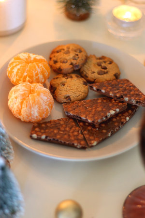 Various Christmas decorations, cookies, chocolate, nuts and tangerines, wine glasses and lit candles...