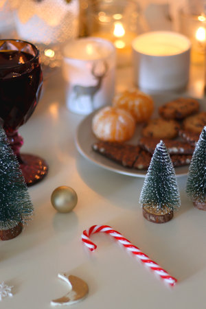 Various Christmas decorations, cookies, chocolate, nuts and tangerines, wine glasses and lit candles on the table. Holiday hygge at home. Selective focus.の写真素材