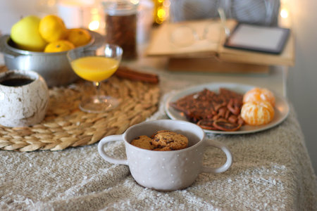 Books, e-reader, tea, orange juice, fruit, snacks, yarn, blanket and lit candles on the table. Autumn or winter hygge at home. Selective focus.の写真素材