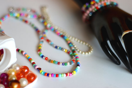 Hand figurine, colorful friendship bracelets, necklaces, various beads and DIY supplies on the table. Making jewelry at home. Selective focus.の写真素材