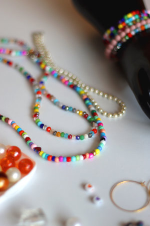 Hand figurine, colorful friendship bracelets, necklaces, various beads and DIY supplies on the table. Making jewelry at home. Selective focus.の写真素材