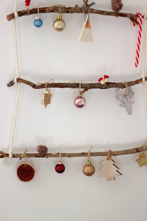 Creative DIY Christmas tree made with branches and decorated with various Christmas ornaments, hanging on the wall.の写真素材
