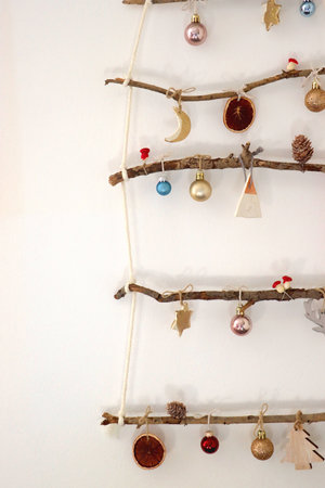 Creative DIY Christmas tree made with branches and decorated with various Christmas ornaments, hanging on the wall.の写真素材