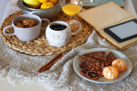 Books, e-reader, tea, orange juice, fruit, snacks, yarn, blanket and lit candles on the table. Autumn or winter hygge at home. Selective focus.の写真素材
