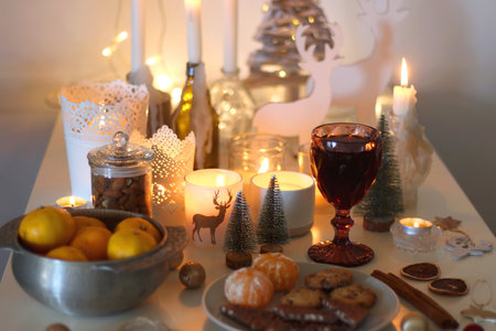 Various Christmas decorations, cookies, chocolate, nuts and tangerines, wine glasses and lit candles on the table. Holiday hygge at home. Selective focus.の写真素材