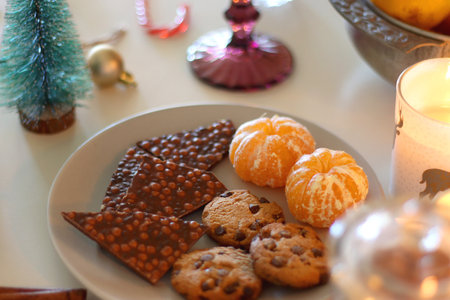 Various Christmas decorations, cookies, chocolate, nuts and tangerines, wine glasses and lit candles on the table. Holiday hygge at home. Selective focus.の写真素材