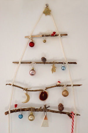 Creative DIY Christmas tree made with branches and decorated with various Christmas ornaments, hanging on the wall.の写真素材