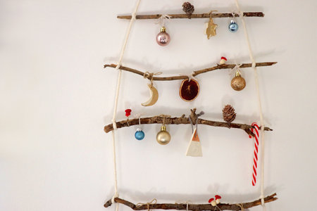 Creative DIY Christmas tree made with branches and decorated with various Christmas ornaments, hanging on the wall.の写真素材