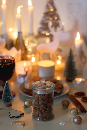 Various Christmas decorations, cookies, chocolate, nuts and tangerines, wine glasses and lit candles on the table. Holiday hygge at home. Selective focus.の写真素材