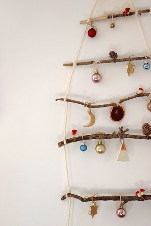 Creative DIY Christmas tree made with branches and decorated with various Christmas ornaments, hanging on the wall.の写真素材