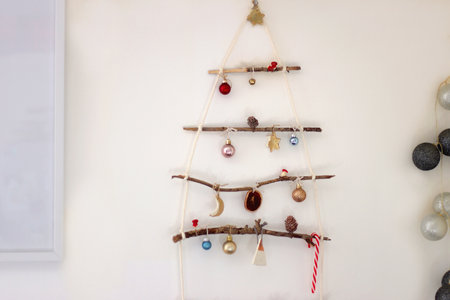 Creative DIY Christmas tree made with branches and decorated with various Christmas ornaments, hanging on the wall.の写真素材