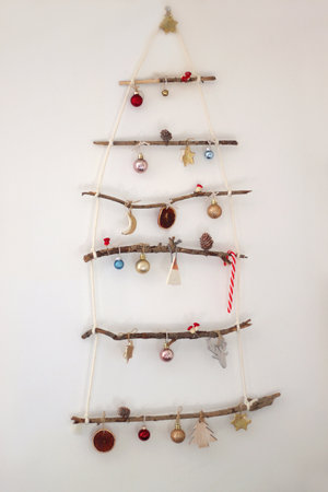 Creative DIY Christmas tree made with branches and decorated with various Christmas ornaments, hanging on the wall.の写真素材