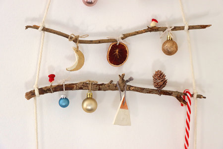Creative DIY Christmas tree made with branches and decorated with various Christmas ornaments, hanging on the wall.の写真素材