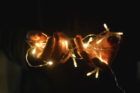Hands holding fairy lights in the dark. Selective focus.