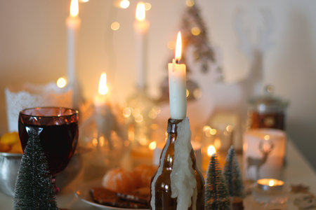 Various Christmas decorations, cookies, chocolate, nuts and tangerines, wine glasses and lit candles on the table. Holiday hygge at home. Selective focus.の写真素材