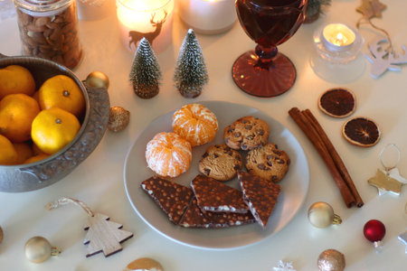 Various Christmas decorations, cookies, chocolate, nuts and tangerines, wine glasses and lit candles on the table. Holiday hygge at home. Selective focus.の写真素材