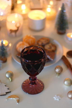Various Christmas decorations, cookies, chocolate, nuts and tangerines, wine glasses and lit candles on the table. Holiday hygge at home. Selective focus.の写真素材