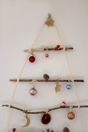 Creative DIY Christmas tree made with branches and decorated with various Christmas ornaments, hanging on the wall.の写真素材
