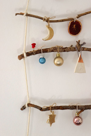 Creative DIY Christmas tree made with branches and decorated with various Christmas ornaments, hanging on the wall.の写真素材
