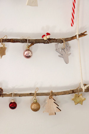 Creative DIY Christmas tree made with branches and decorated with various Christmas ornaments, hanging on the wall.の写真素材