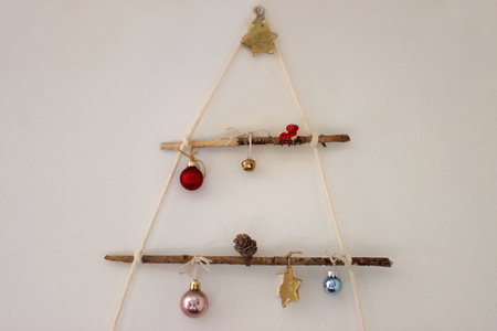 Creative DIY Christmas tree made with branches and decorated with various Christmas ornaments, hanging on the wall.の写真素材