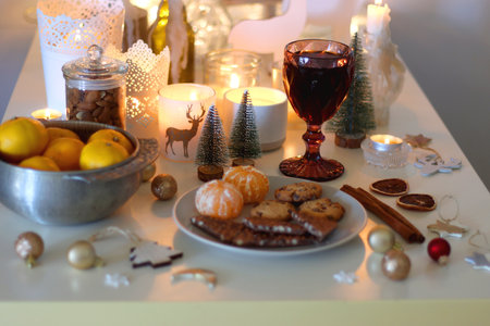 Various Christmas decorations, cookies, chocolate, nuts and tangerines, wine glasses and lit candles on the table. Holiday hygge at home. Selective focus.の写真素材