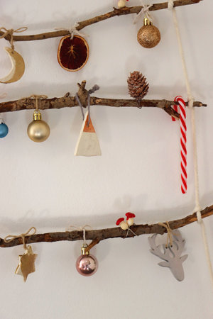 Creative DIY Christmas tree made with branches and decorated with various Christmas ornaments, hanging on the wall.の写真素材