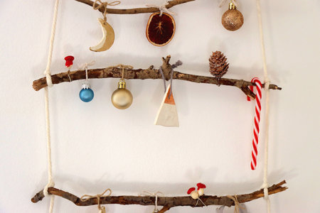 Creative DIY Christmas tree made with branches and decorated with various Christmas ornaments, hanging on the wall.の写真素材