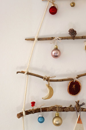 Creative DIY Christmas tree made with branches and decorated with various Christmas ornaments, hanging on the wall.の写真素材