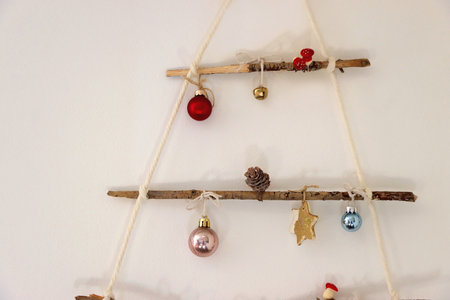 Creative DIY Christmas tree made with branches and decorated with various Christmas ornaments, hanging on the wall.の写真素材
