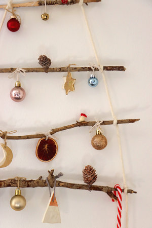 Creative DIY Christmas tree made with branches and decorated with various Christmas ornaments, hanging on the wall.の写真素材