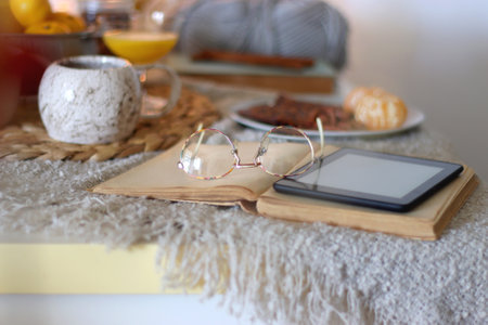 Books, e-reader, orange juice, fruit, snacks, and a tablet on the table. Autumn or winter hygge at...