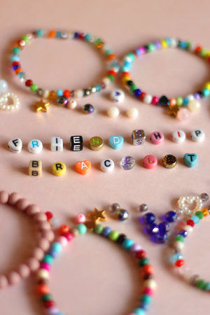 Friendship bracelet spelled with letter beads. Colorful handmade bracelets and various beads. Top view, pink background.の写真素材
