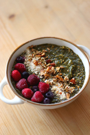 Beige bowl with green smoothie, frozen berries and homemade granola, served on the table. Selective focus.の写真素材